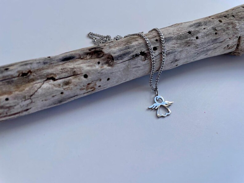 May include: A silver chain necklace with a small angel pendant. The pendant is a cutout design of an angel with wings.