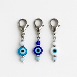 Pu&ograve; includere: Tre ciondoli con chiusure argentate. Ogni ciondolo presenta un design di perline di vetro con un motivo a occhio greco. Le perline sono in tonalit&agrave; di blu e bianco, con accenti argentati. I ciondoli sono progettati per la creazione di gioielli o come accessori decorativi.