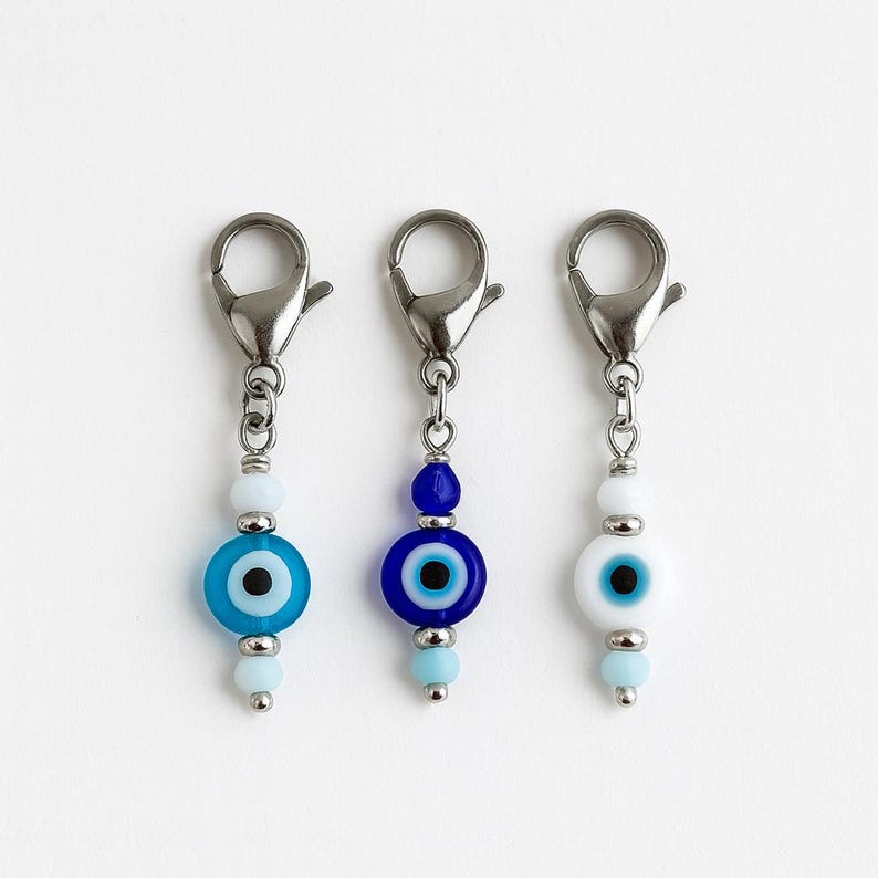 Pu&ograve; includere: Tre ciondoli con chiusure argentate. Ogni ciondolo presenta un design di perline di vetro con un motivo a occhio greco. Le perline sono in tonalit&agrave; di blu e bianco, con accenti argentati. I ciondoli sono progettati per la creazione di gioielli o come accessori decorativi.