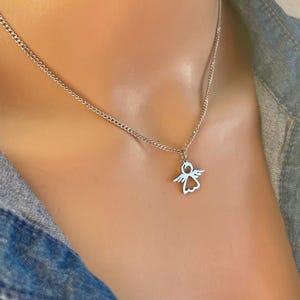 May include: A silver chain necklace with a small angel pendant. The angel is cut out of the metal, creating a delicate silhouette.