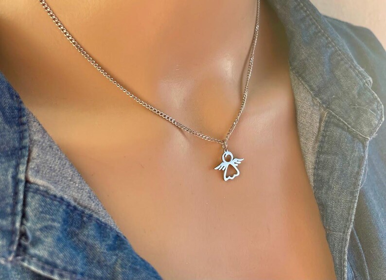 May include: A silver chain necklace with a small angel pendant. The angel is cut out of the metal, creating a delicate silhouette.