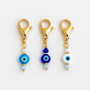 Pu&ograve; includere: Tre chiusure a ciondolo color oro con perline a forma di occhio diabolico. Le perline sono blu e bianche, con dettagli dorati. Le chiusure sono progettate per la creazione di gioielli o per il fissaggio ad accessori.