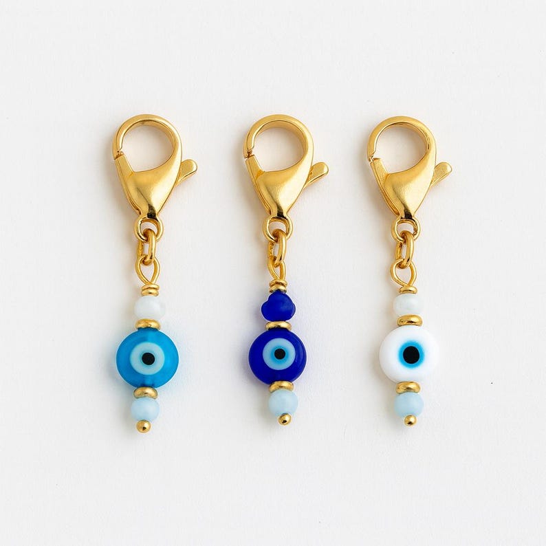 Pu&ograve; includere: Tre chiusure a ciondolo color oro con perline a forma di occhio diabolico. Le perline sono blu e bianche, con dettagli dorati. Le chiusure sono progettate per la creazione di gioielli o per il fissaggio ad accessori.