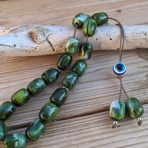 Op de afbeelding: Groene en witte marmerachtige gebedskralen met een blauwe en witte boze oog-hanger aan een bruin koord.