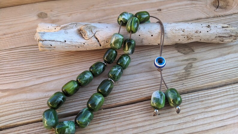 Op de afbeelding: Groene en witte marmerachtige gebedskralen met een blauwe en witte boze oog-hanger aan een bruin koord.