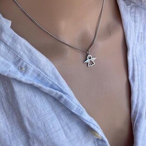 May include: A silver chain necklace with a small angel pendant. The angel is a simple outline with wings and a halo.