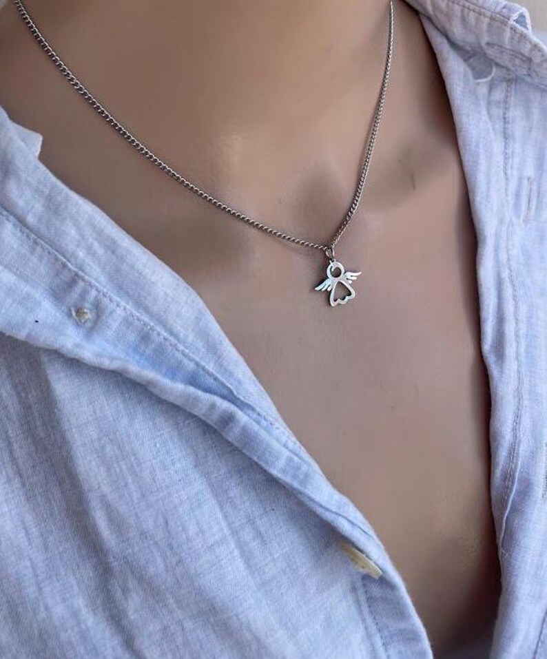 May include: A silver chain necklace with a small angel pendant. The angel is a simple outline with wings and a halo.
