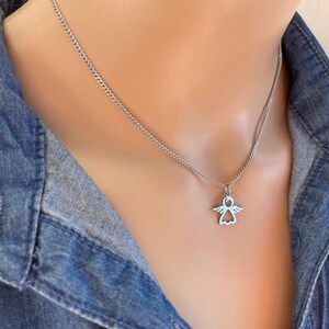 May include: A silver chain necklace with a small angel pendant. The angel is a simple outline with wings and a halo.