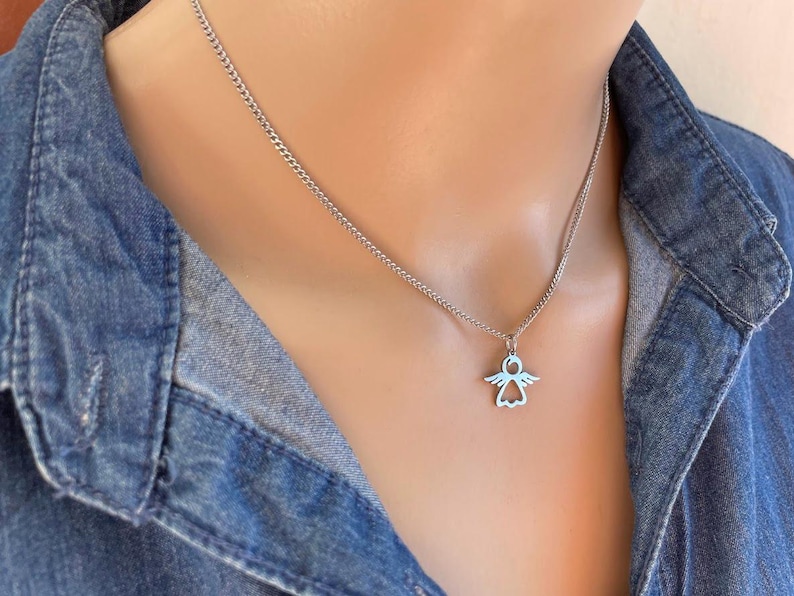 May include: A silver chain necklace with a small angel pendant. The angel is a simple outline with wings and a halo.