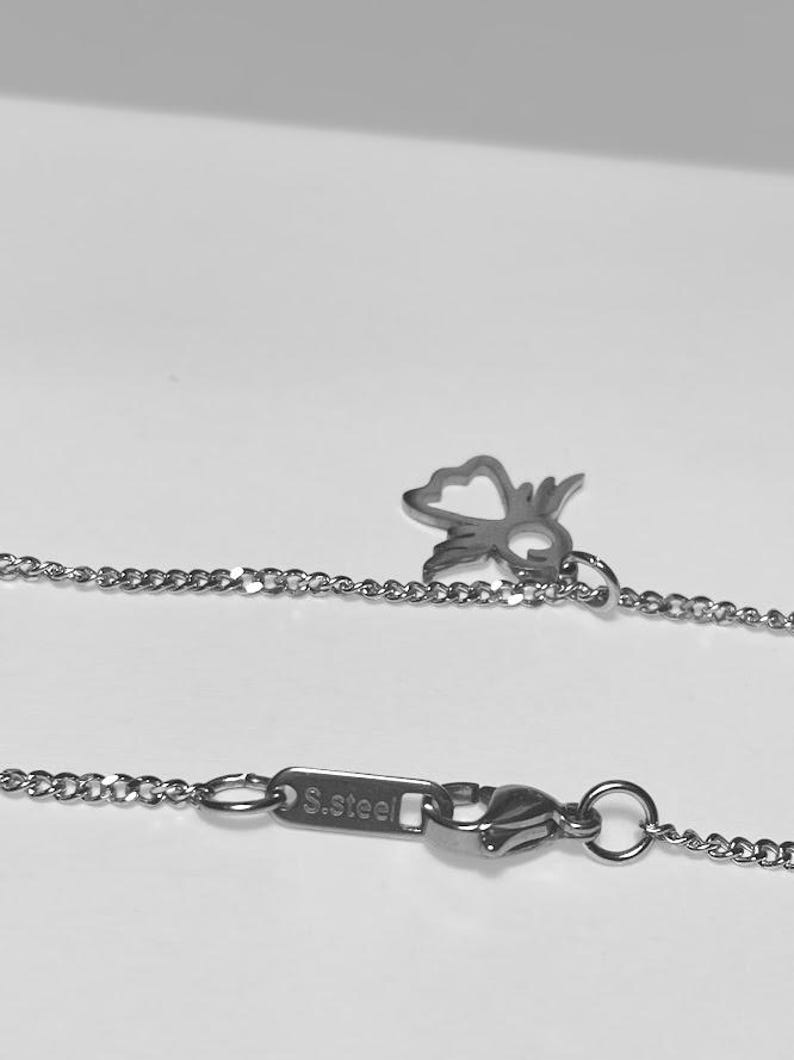 May include: A silver chain necklace with a small, open heart charm and a lobster clasp. The clasp has a tag that reads "S.Steel".