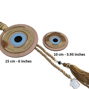 May include: Two wooden evil eye wall hangings with gold trim and blue eyes. The larger one is 6 inches in diameter and the smaller one is 3.93 inches in diameter. Both have Greek text around the eye that says "tychi", "ygeia", "eutychia", and "agapi".