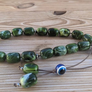 Op de afbeelding: Groene en witte marmerachtige gebedskralen met een blauwe en witte boze oog-hanger aan een bruin koord.