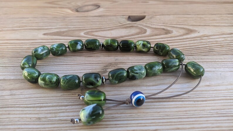 Op de afbeelding: Groene en witte marmerachtige gebedskralen met een blauwe en witte boze oog-hanger aan een bruin koord.