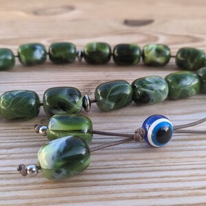 Op de afbeelding: Groene en witte marmerachtige gebedskralen met een blauwe en witte boze oog charme.