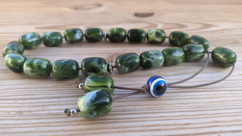 Op de afbeelding: Groene en witte marmerachtige gebedskralen met een blauwe en witte boze oog charme.