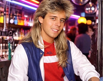 May include: A person wearing a white and blue jacket over a red shirt with the word "JO" visible. The person is smiling, with long, light-colored hair. The background includes disco balls and neon lights, suggesting a retro theme.