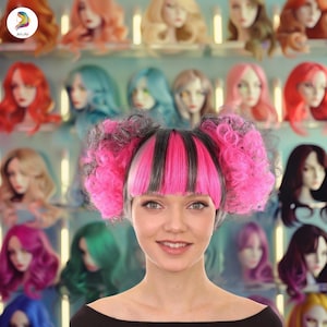 May include: A woman with pink and black pigtails smiles in front of a display of wigs. The pigtails have a fringe and are styled with a mix of pink and black hair. The background features various wigs in different colors.
