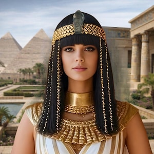May include: A woman in an Egyptian-inspired costume. She wears a gold headdress with a snake emblem, a gold collar, and a white and gold top. Her black hair is adorned with gold beads. The background features pyramids and ancient architecture.