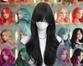 May include: A black wig with long, flowing hair and bangs, styled on a mannequin head. The wig is secured with two small clips. A silver necklace is around the mannequin's neck. Other colorful wigs are visible in the background.