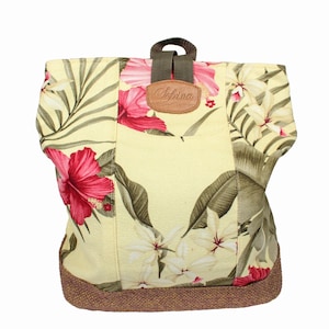 May include: A yellow canvas backpack with a floral print featuring pink hibiscus flowers and green leaves. The backpack has a brown leather patch with the word "Adina" on it.