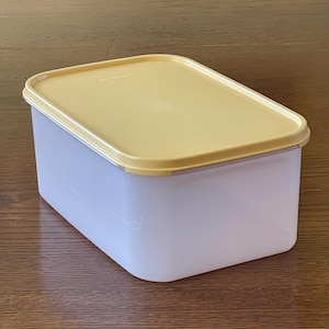 May include: A rectangular, translucent plastic container with a yellow lid. The container has a slightly rounded base and straight sides. The lid fits snugly on top, creating a secure seal. The container is designed for food storage.