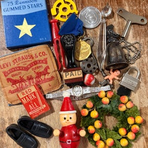 May include: A collection of vintage items including a blue box of gummed stars, a Levi Strauss leather patch, a red stamp, a silver watch, a Santa Claus figure, a small wreath, a metal bell, a padlock, a key, and a pair of black shoes.