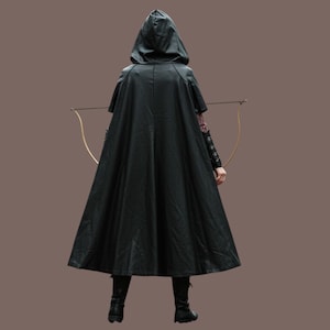 May include: A person wearing a black hooded cloak and holding a bow and arrow. The cloak is long and flowing, and the hood is pulled up over the person's head.