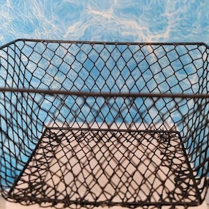 May include: A black wire mesh basket with a square shape. The basket is empty and has a wire mesh bottom.