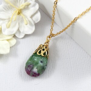 May include: A gold chain necklace with a green and pink teardrop-shaped gemstone pendant. The pendant is set in a gold filigree frame.