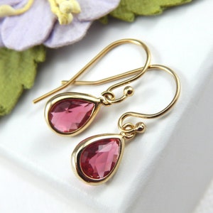 May include: A pair of gold dangle earrings with pink teardrop-shaped gemstones.