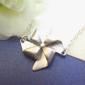 May include: A silver necklace with a silver wind spinner charm. The wind spinner is shaped like a four-pointed star with a bow in the center.