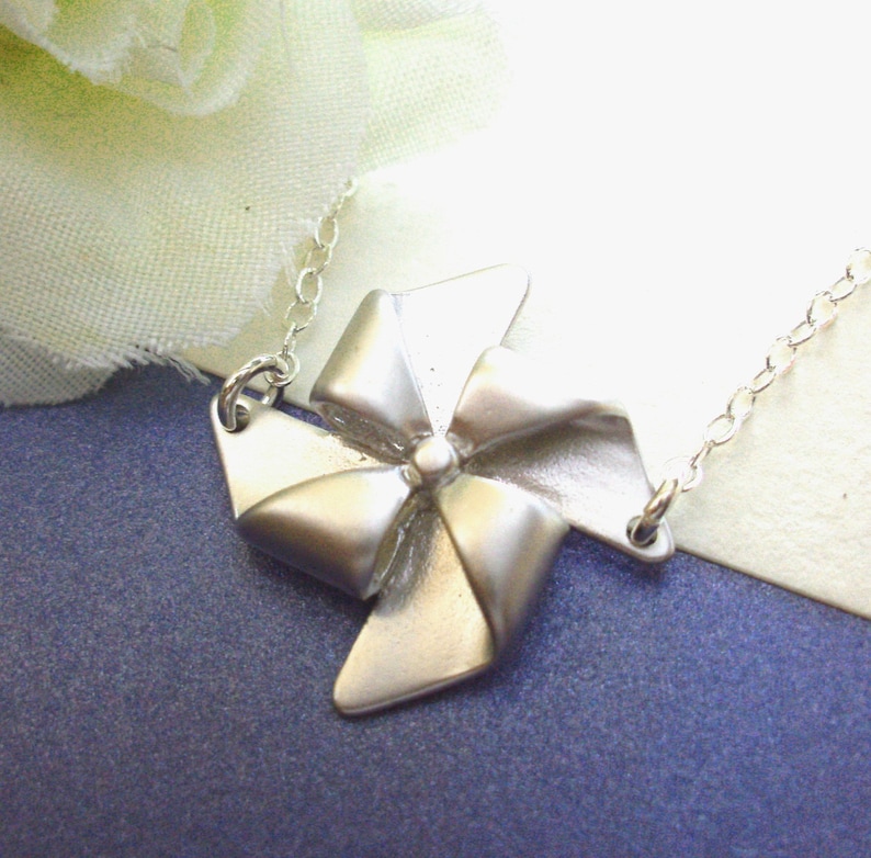 May include: A silver necklace with a silver wind spinner charm. The wind spinner is shaped like a four-pointed star with a bow in the center.