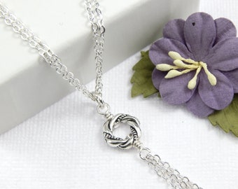 May include: A silver necklace with a twisted circle pendant and multiple chain strands.
