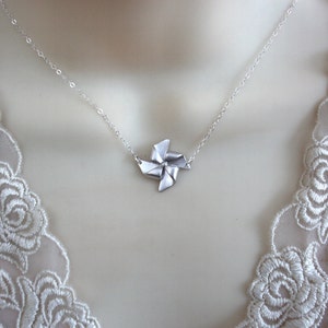 May include: A silver necklace with a delicate silver windmill pendant. The necklace is on a white lace background.