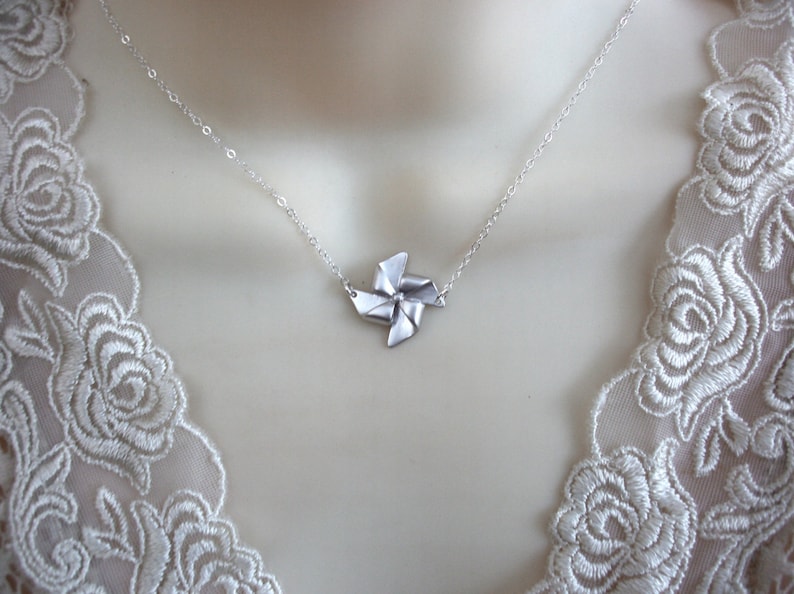 May include: A silver necklace with a delicate silver windmill pendant. The necklace is on a white lace background.