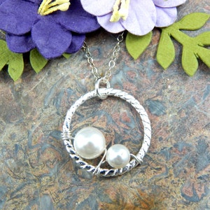 May include: A silver necklace with a twisted circle pendant featuring two white pearls. The pendant is on a silver chain.