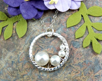 May include: A silver necklace with a twisted wire circle pendant featuring three white pearls. The pendant is surrounded by a twisted wire design.