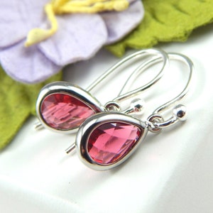 May include: A pair of silver dangle earrings with teardrop-shaped pink crystal stones.