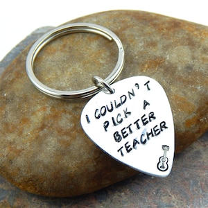 May include: A silver guitar pick keyring with the words "I COULDN'T PICK A BETTER TEACHER" in black lettering. A small guitar is etched at the bottom. The keyring is on a silver ring.