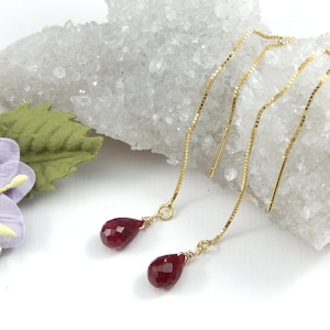 May include: A pair of gold chain earrings with red teardrop-shaped gemstones.