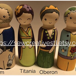 May include: Four hand-painted wooden peg dolls representing characters from A Midsummer Night's Dream. The figures are labeled Bottom, Titania, Oberon, and Puck, and feature detailed clothing in blue, green, purple, and yellow paint.