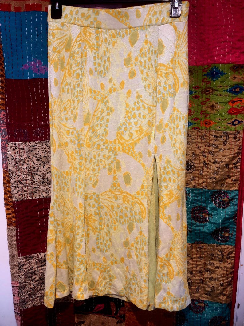 Pode incluir: Uma saia de estampa floral amarela e verde com uma fenda lateral. A saia &eacute; de comprimento at&eacute; o joelho e tem cintura ajustada.