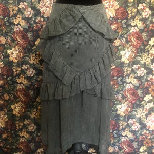 Op de afbeelding: Een zwart-witte polkadot rok met gelaagde ruches. De rok wordt getoond op een zwarte mannequin en heeft een unieke asymmetrische zoom. De stof heeft een subtiele glans en het ontwerp is klassiek en veelzijdig.