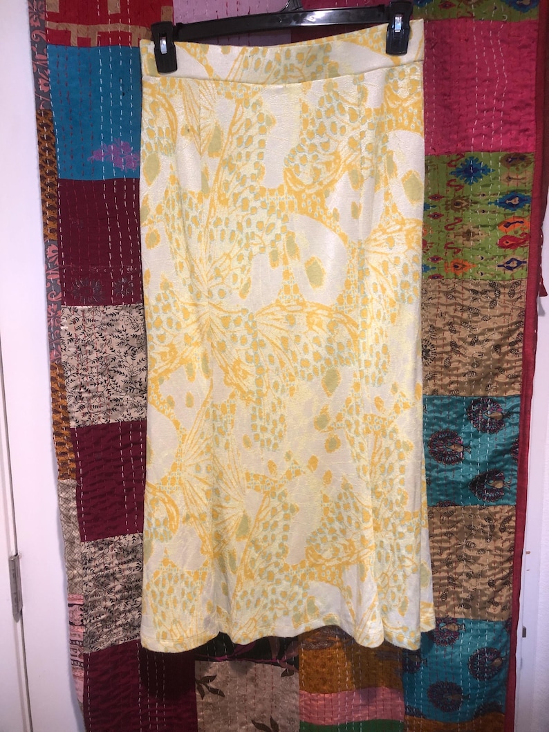 Pode incluir: Uma saia de estampa floral amarela e branca com cintura alta e comprimento midi.