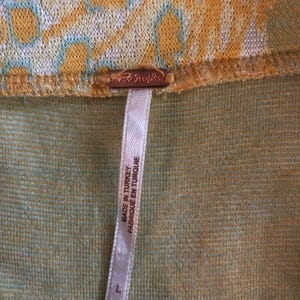 Pode incluir: Uma etiqueta branca com texto preto que diz "Made in Turkey Fabrique en Turquie" anexada a um tecido estampado amarelo e verde. A etiqueta tem um tamanho "L" impresso.