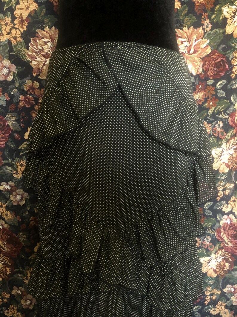 Op de afbeelding: Zwarte rok met witte stippen en gelaagde ruches. De rok heeft een hoge taille en een getailleerd silhouet. De stof lijkt een lichtgewicht materiaal te zijn, geschikt voor warmer weer. De rok is een klassiek en veelzijdig kledingstuk.