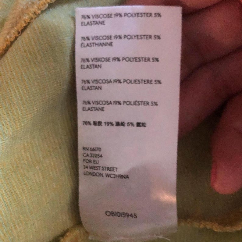 Pode incluir: Uma etiqueta branca com texto preto que detalha a composi&ccedil;&atilde;o do tecido de uma pe&ccedil;a de roupa. A etiqueta indica que o tecido &eacute; composto por 76% viscose, 19% poli&eacute;ster e 5% elastano. A etiqueta tamb&eacute;m inclui os n&uacute;meros RN e CA da marca, bem como o endere&ccedil;o da empresa em Londres, Inglaterra. A etiqueta tem um n&uacute;mero de identifica&ccedil;&atilde;o &uacute;nico: OB1015945.