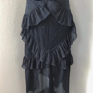 Op de afbeelding: Een zwart-witte polkadot rok met gelaagde ruches. De rok is gemaakt van een doorschijnende stof en heeft een hoge taille. De rok wordt getoond op een zwarte mannequin.