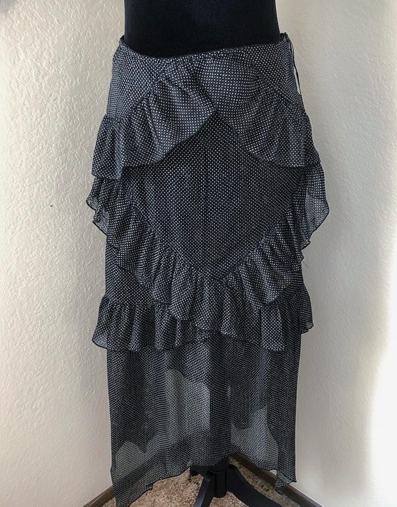 Op de afbeelding: Een zwart-witte polkadot rok met gelaagde ruches. De rok is gemaakt van een doorschijnende stof en heeft een hoge taille. De rok wordt getoond op een zwarte mannequin.