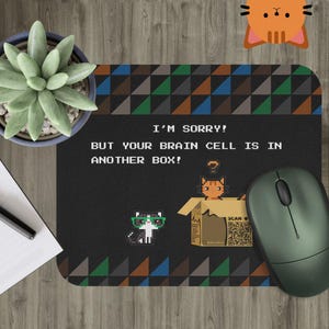 May include: Black mousepad with a pixelated cat design and the text "I'M SORRY! BUT YOUR BRAIN CELL IS IN ANOTHER BOX!". Features a green mouse and a succulent plant in a blue pot.